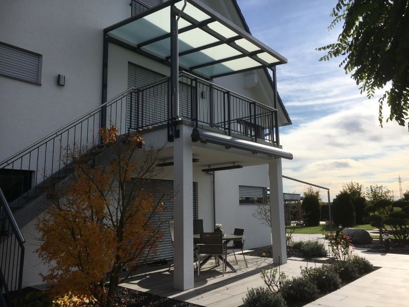 Außenansicht eines weißen Hauses mit Balkon, Treppe und Metalldach. Sonniger Tag.