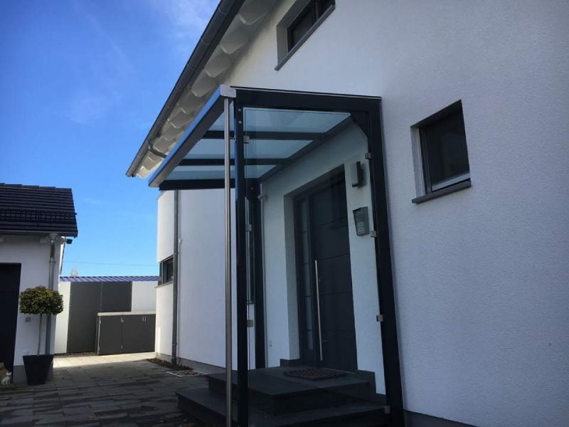 Schwarze und gläserne Markise über der Haustür, weißes Haus, blauer Himmel.