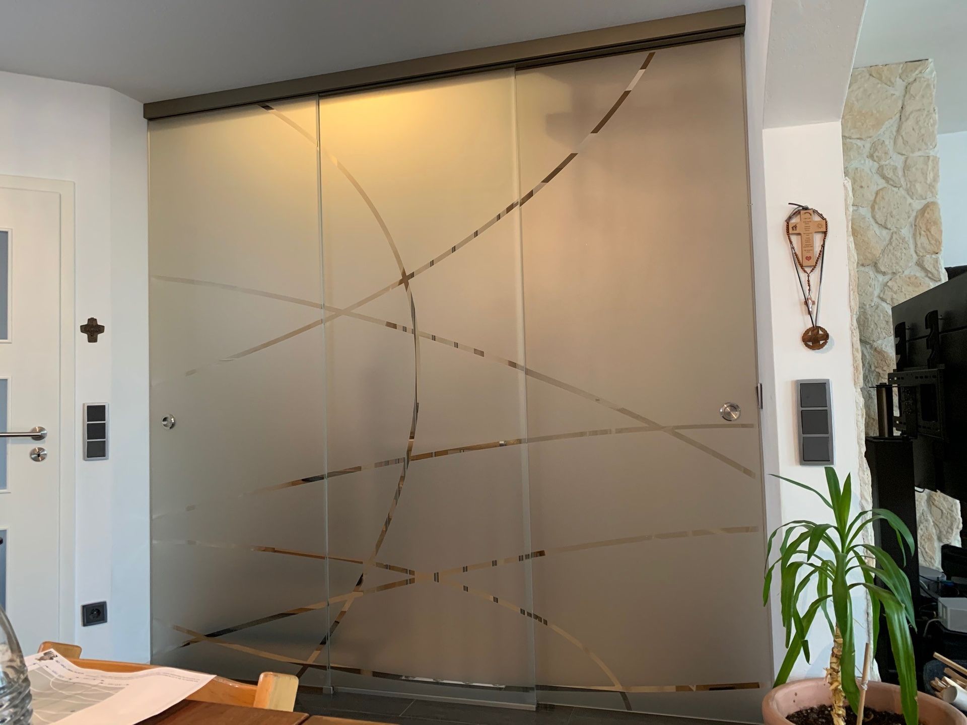 Holztüren aus Glas mit schwarzen Griffen spiegeln eine Terrasse mit Sitzgelegenheiten und den Blick auf Bäume und Himmel wider.