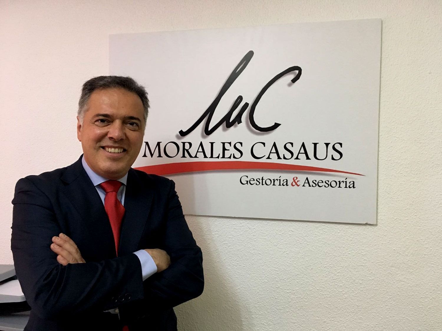 Un hombre con traje y corbata está parado frente a un cartel que dice morales casaus