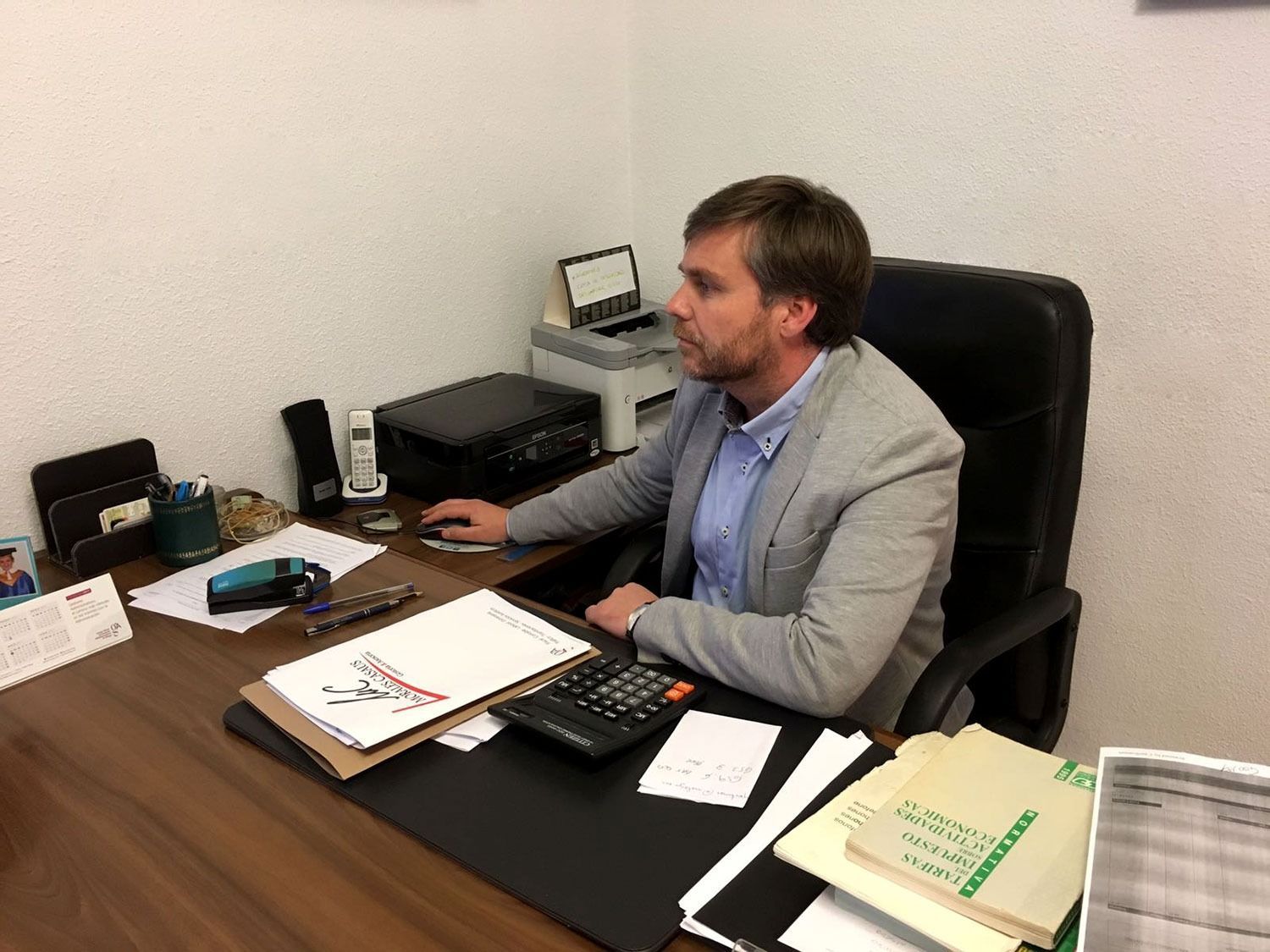 Un hombre está sentado en un escritorio con una calculadora y una impresora.