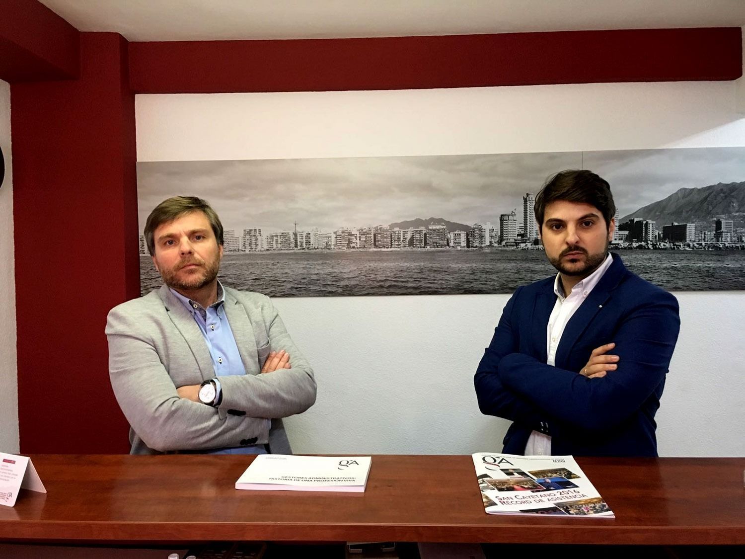 Dos hombres están de pie uno al lado del otro en un escritorio con los brazos cruzados.
