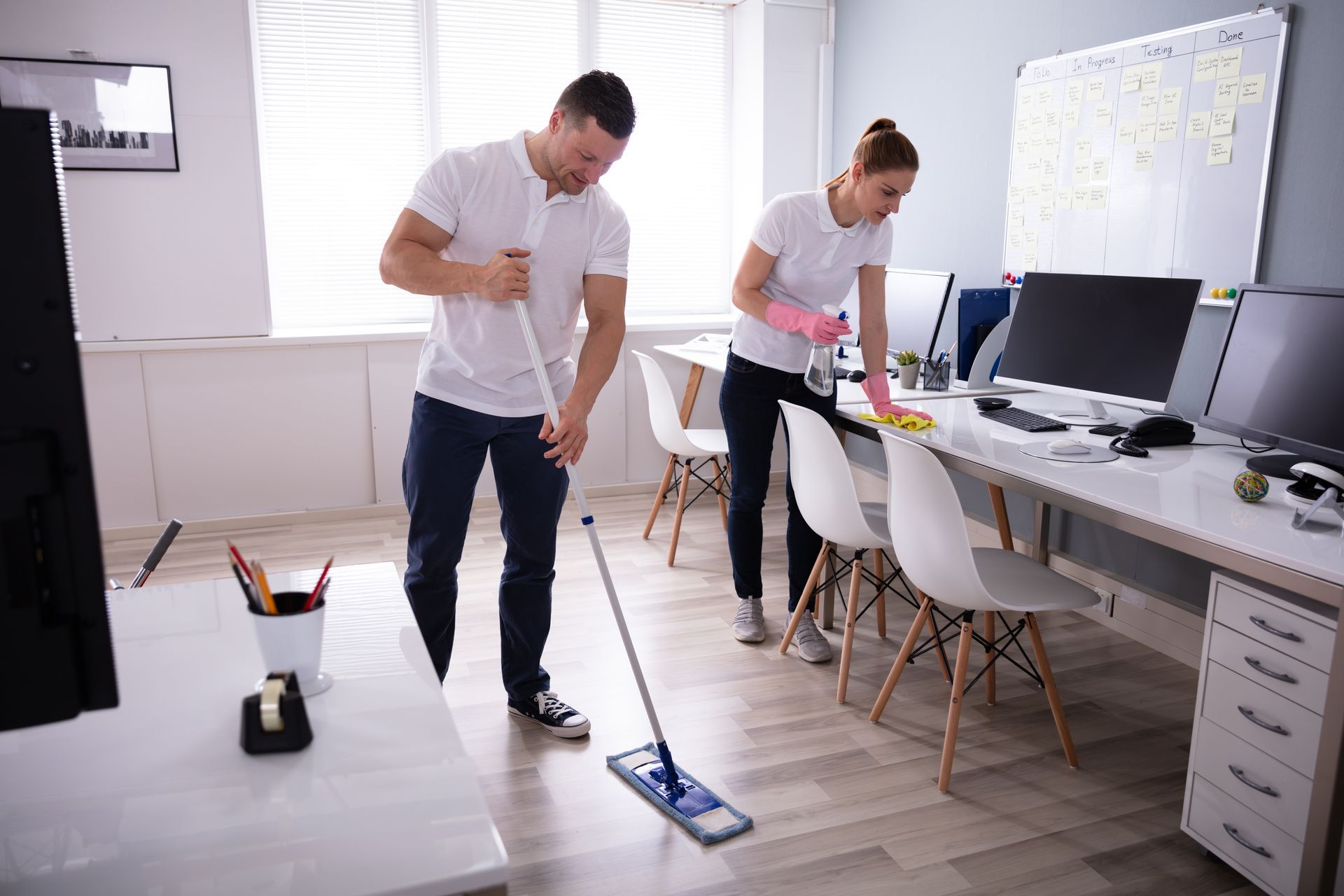 Ein Mann und eine Frau reinigen ein Büro mit einem Wischmopp.
