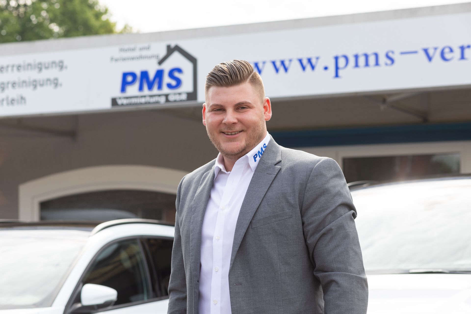 Ein Mann im Anzug steht vor einem Gebäude mit der Aufschrift PMS