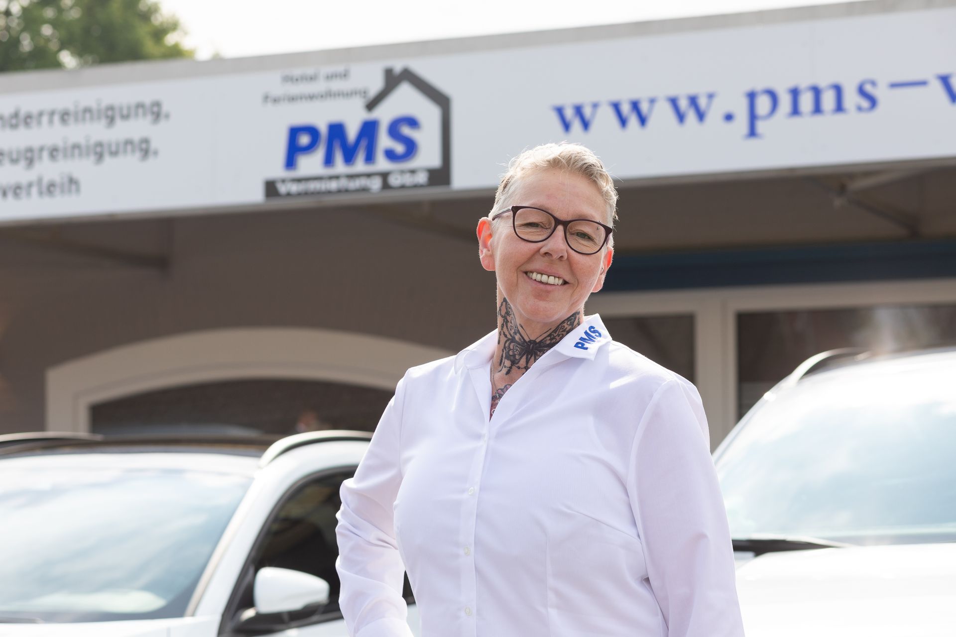 Eine frau im weißen hemd steht vor einem gebäude mit der aufschrift pms.