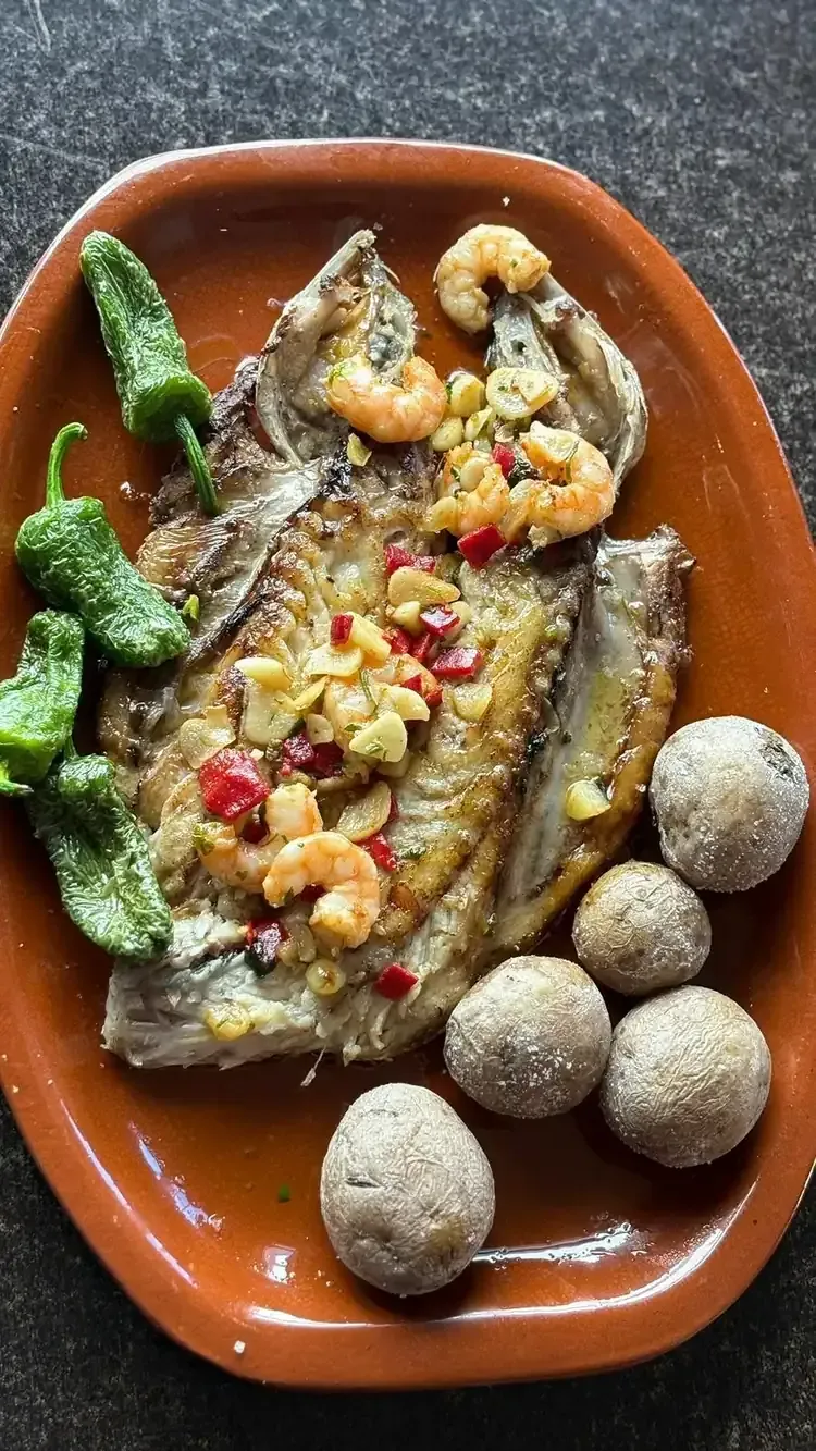 Pescado a la plancha con gambas, pimientos y patatas en plato de terracota.