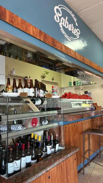 Interior de bar con botellas de vino y cerveza, bocadillos y un cartel que dice “Sabores”.