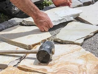 Ein Mann legt mit einem Hammer Steine auf den Boden.