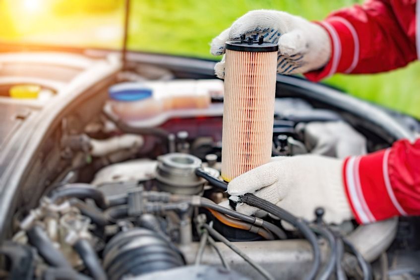 Una persona sostiene un filtro delante del motor de un automóvil.