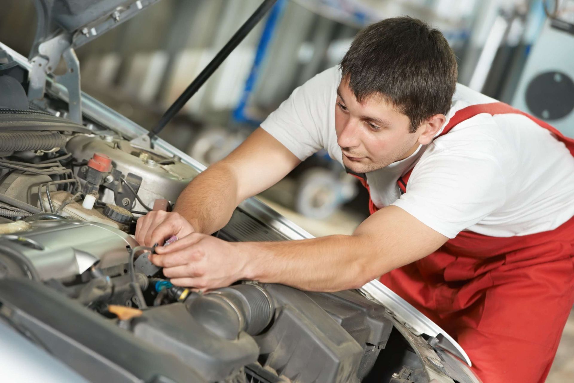Un hombre con un mono rojo está trabajando en el motor de un coche.