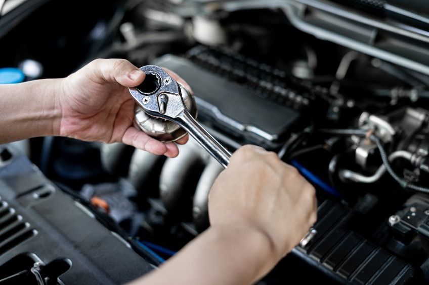 Una persona está trabajando en el motor de un automóvil con una llave inglesa.