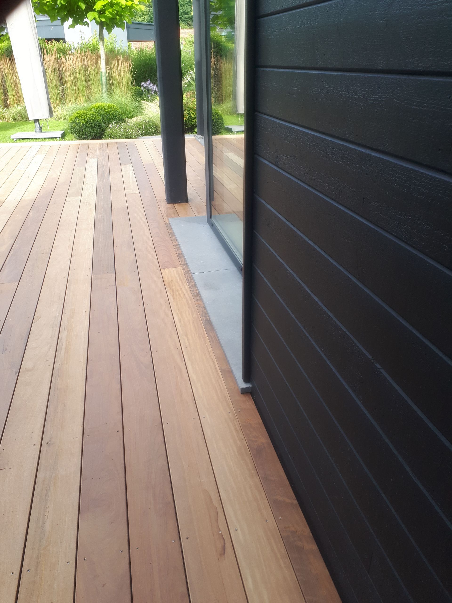 Terrasse en bois à côté d'un bâtiment à panneaux noirs avec une porte vitrée.