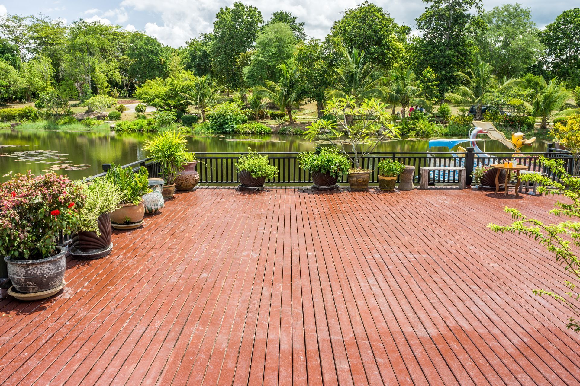 Terrasse en bois avec plantes en pot donnant sur un lac et des arbres verts luxuriants.