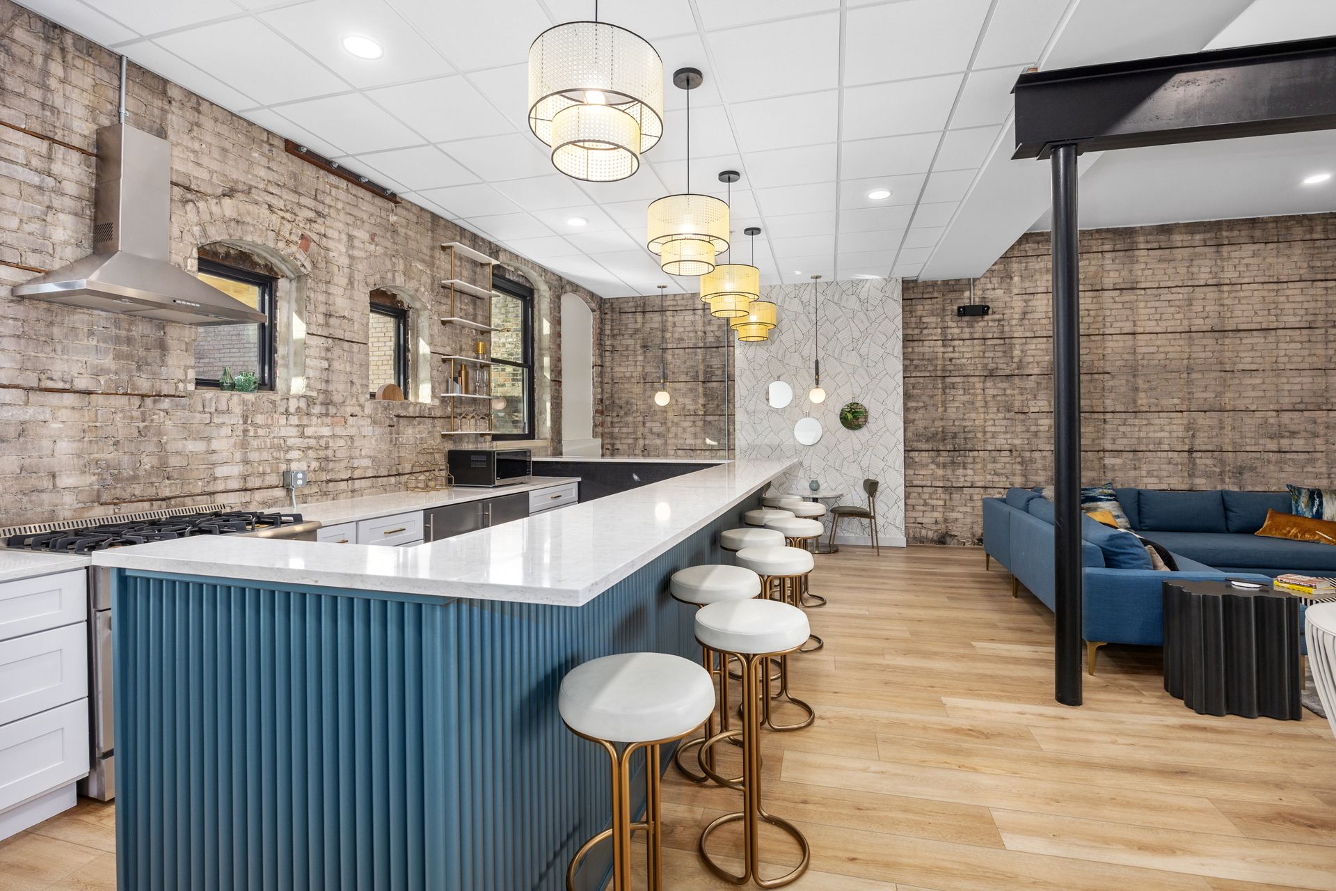 A kitchen with a long counter and stools and a living room with a blue couch.
