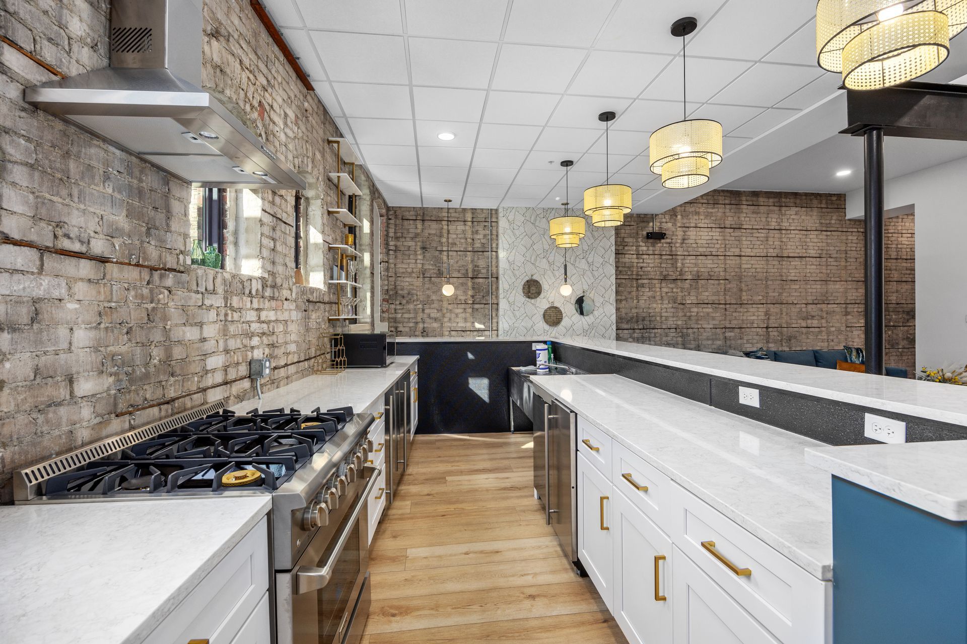 A kitchen with a stove , sink , cabinets and a brick wall.
