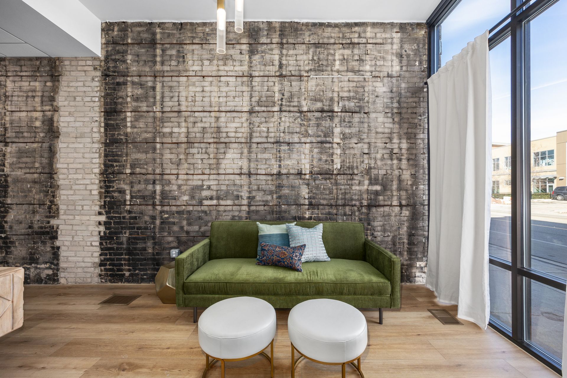 A living room with a green couch and two ottomans in front of a brick wall.