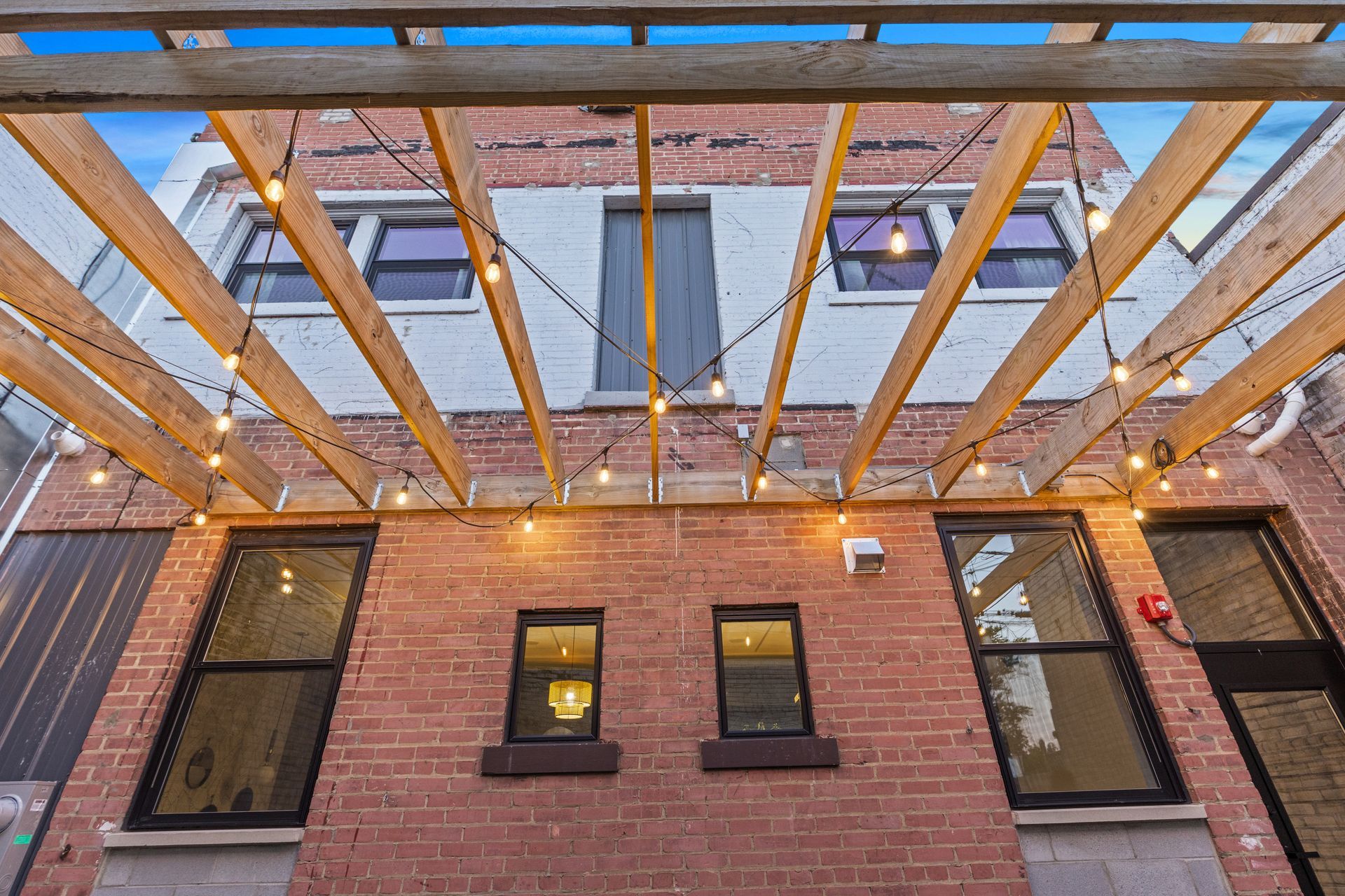 A brick building with a wooden pergola and lights hanging from the ceiling.