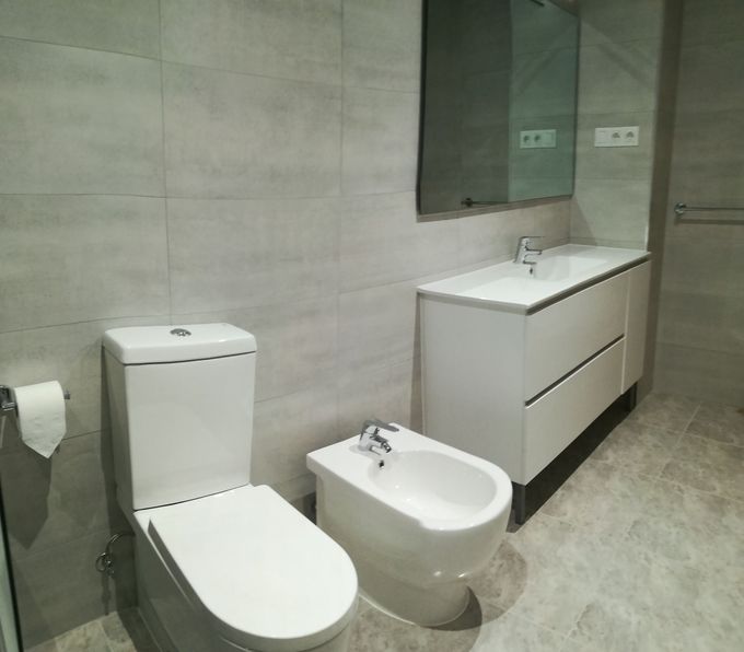 Baño moderno con inodoro, bidé, mueble de lavabo, espejo y paredes revestidas de azulejos grises