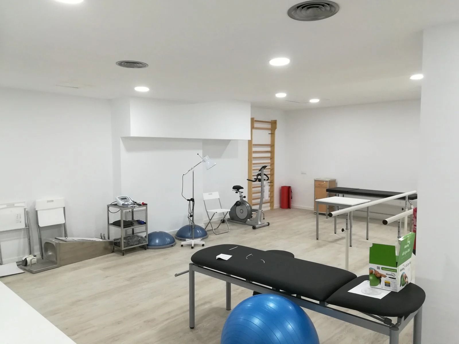 Sala de fisioterapia luminosa, con camillas de tratamiento, equipos de ejercicio y una espaldera