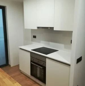 Cocina moderna blanca con horno empotrado, placa de cocina negra y suelo de madera clara