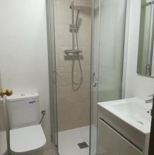 Baño pequeño con inodoro, ducha con mampara de vidrio y lavabo blanco con mueble.