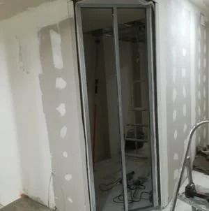 Puerta parcialmente terminada en una habitación en obras, con parches de paneles de yeso y herramientas en el suelo