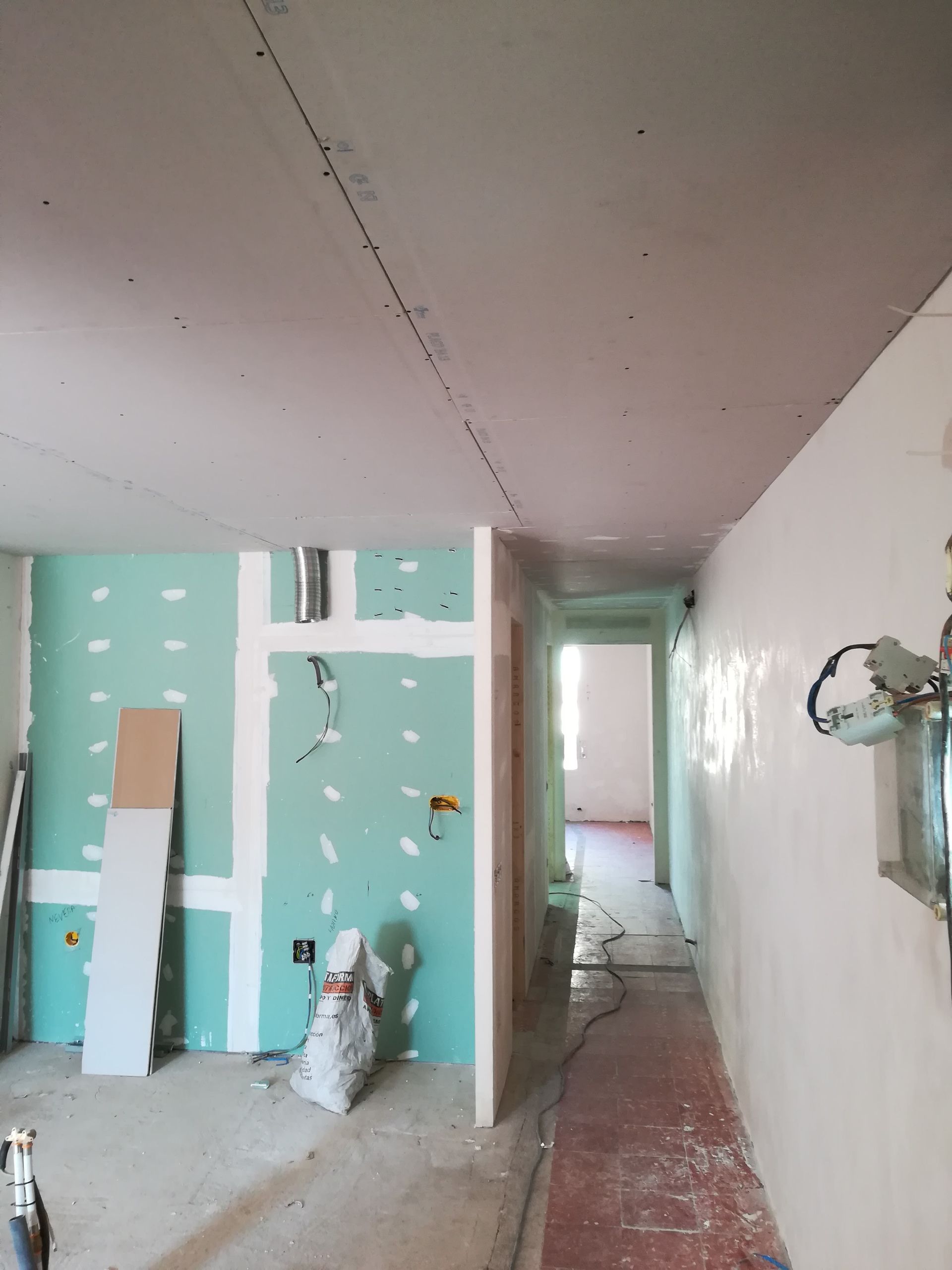 Pasillo parcialmente renovado, con paredes de yeso color verde azulado y blancas, el techo al descubierto