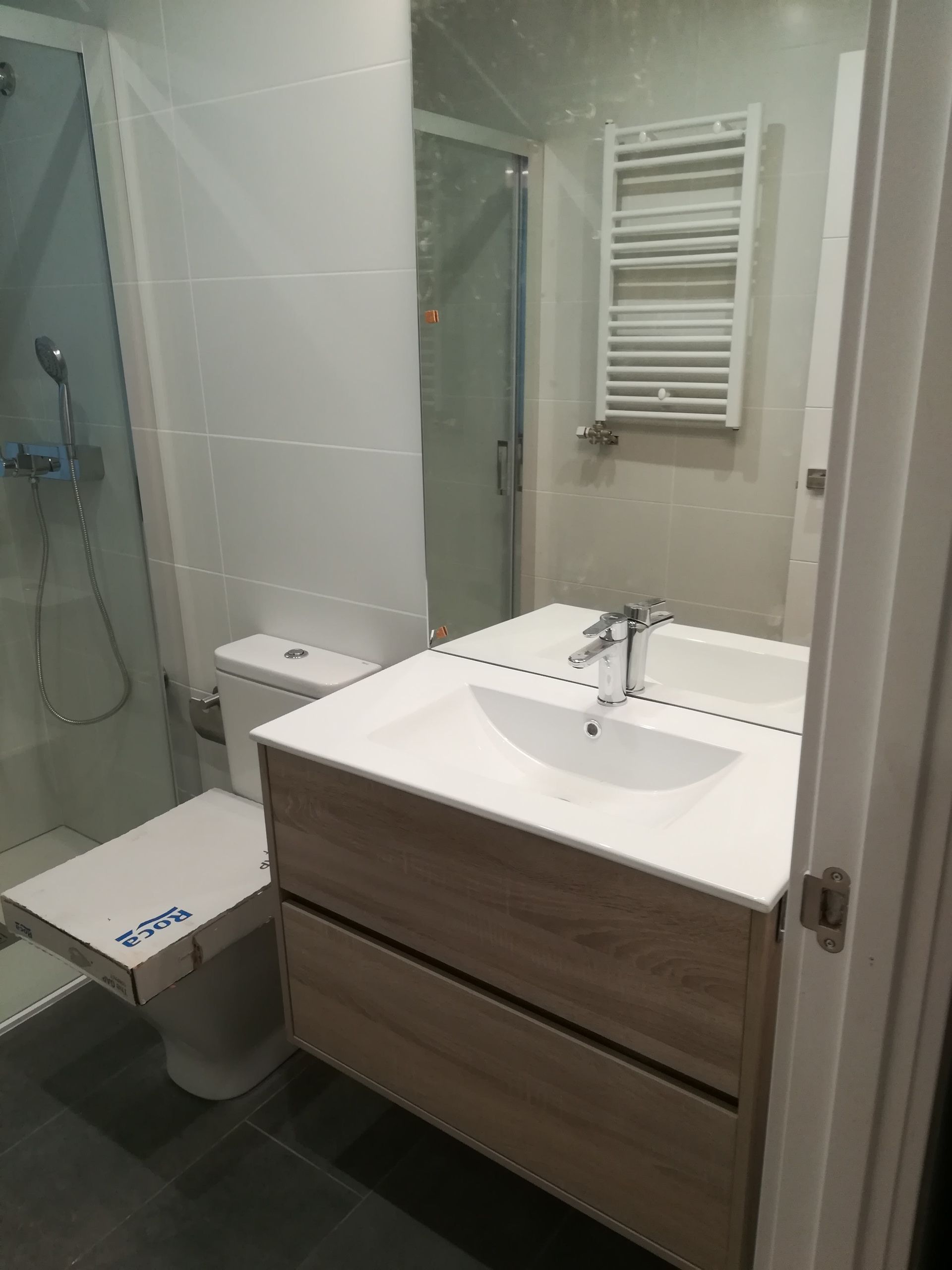 Baño moderno con ducha de cristal, mueble de lavabo blanco, inodoro y radiador toallero