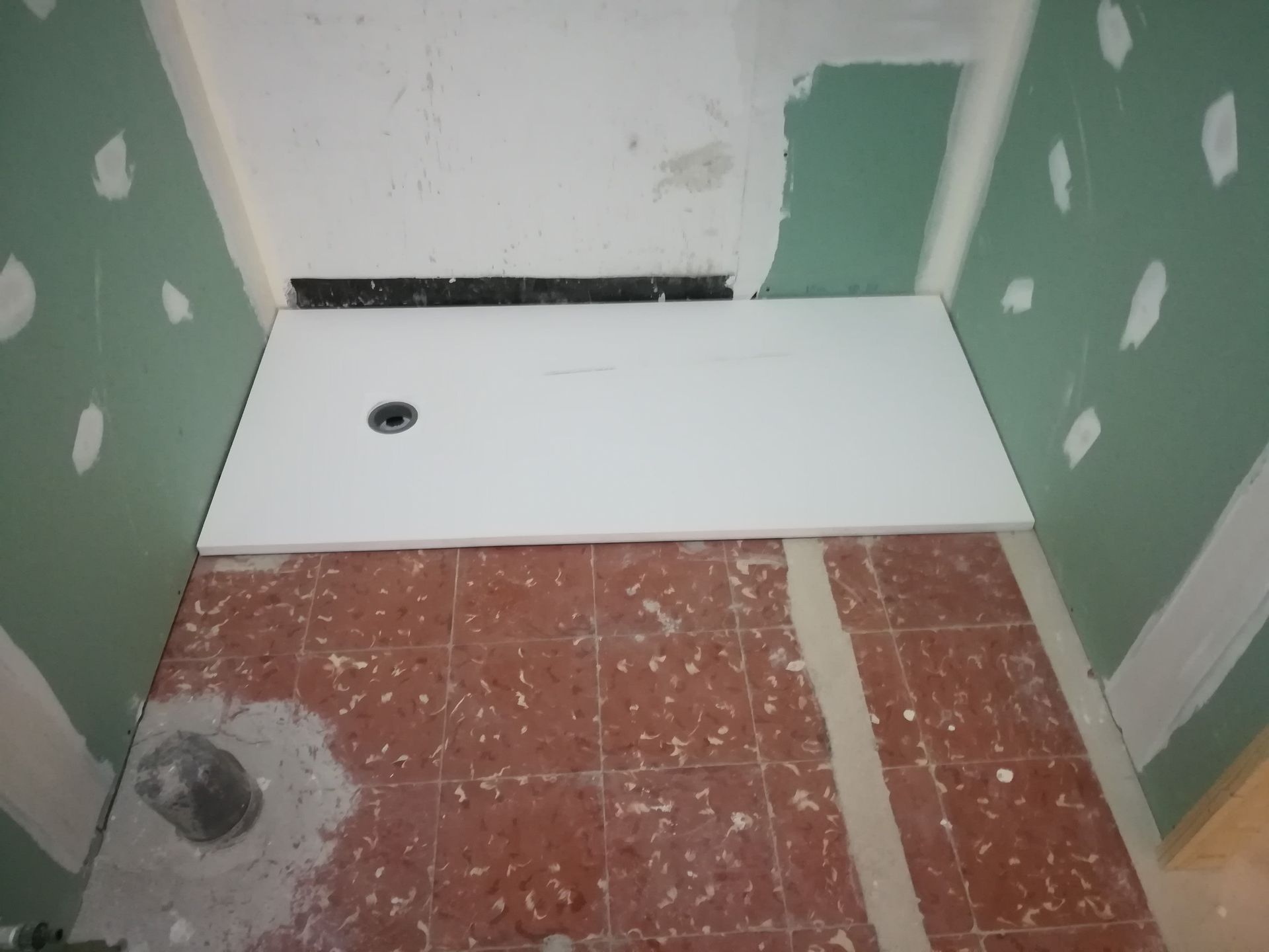 Habitación en renovación, con suelo de baldosas, plato de ducha blanco y paredes verdes con zonas de yeso irregular