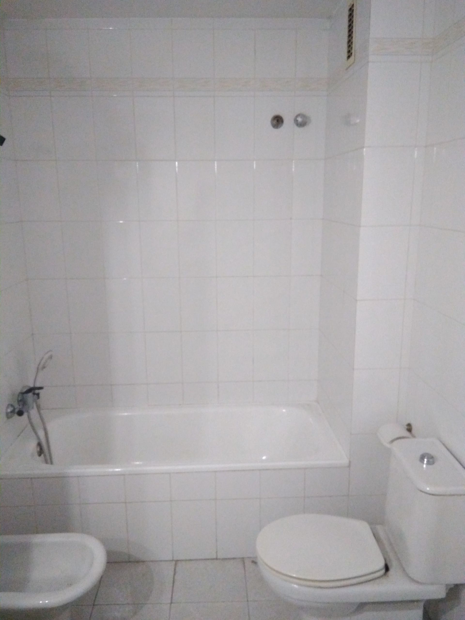 Baño pequeño alicatado con bañera, inodoro y lavabo.