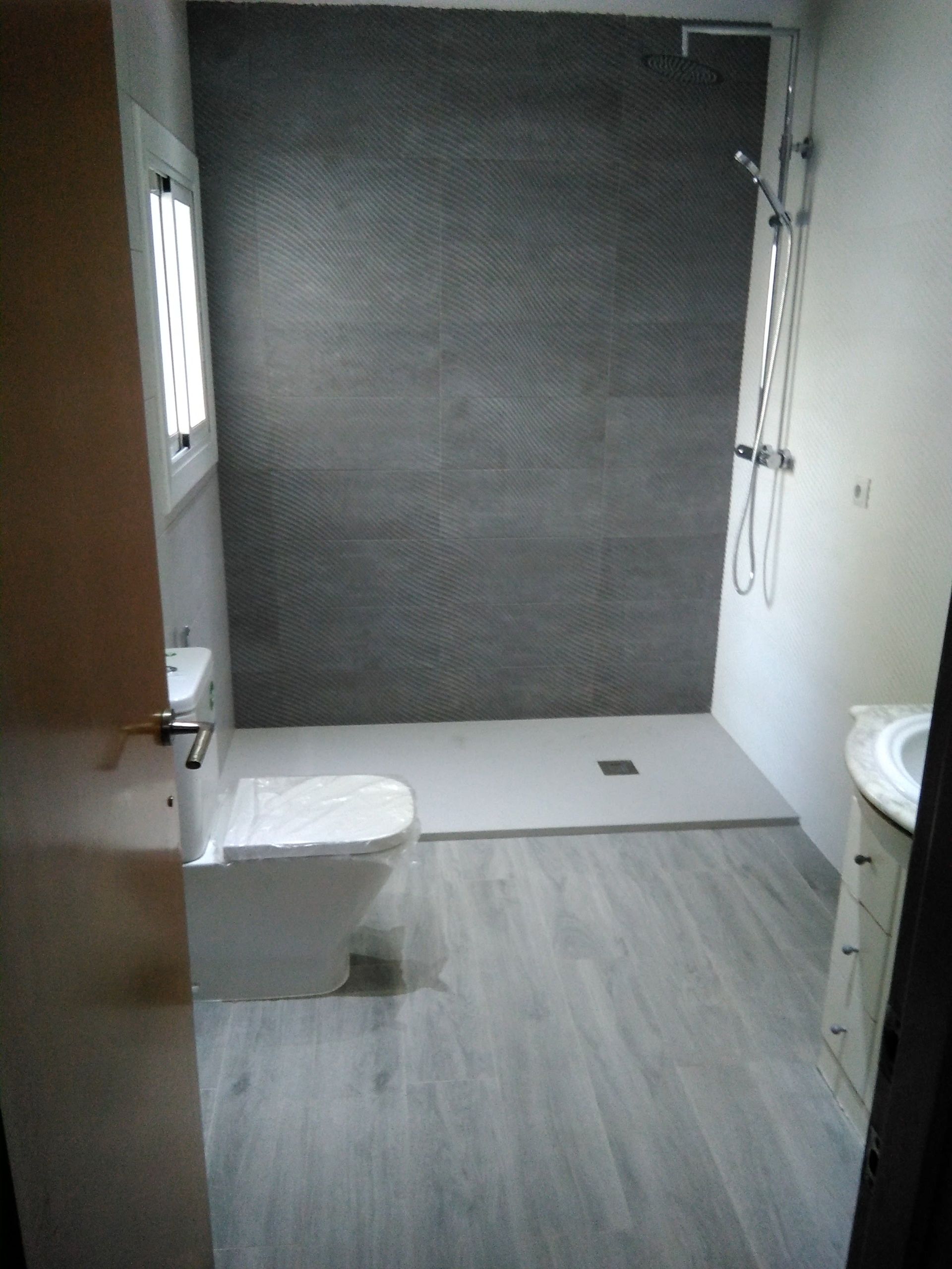 Baño pequeño con ducha, inodoro, lavabo y suelo de baldosas, visto desde la puerta.