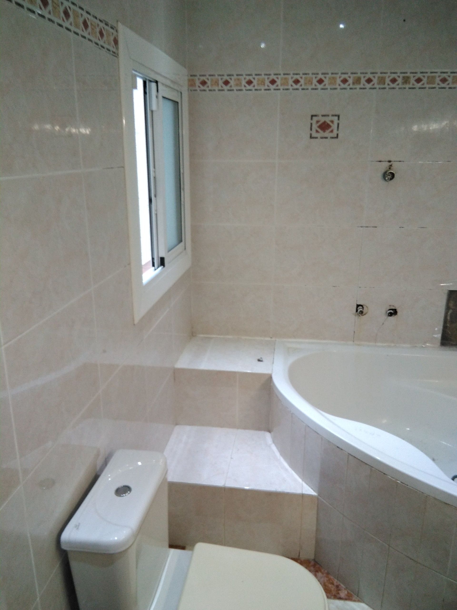 Baño con paredes alicatadas, ventana, inodoro y bañera curva.