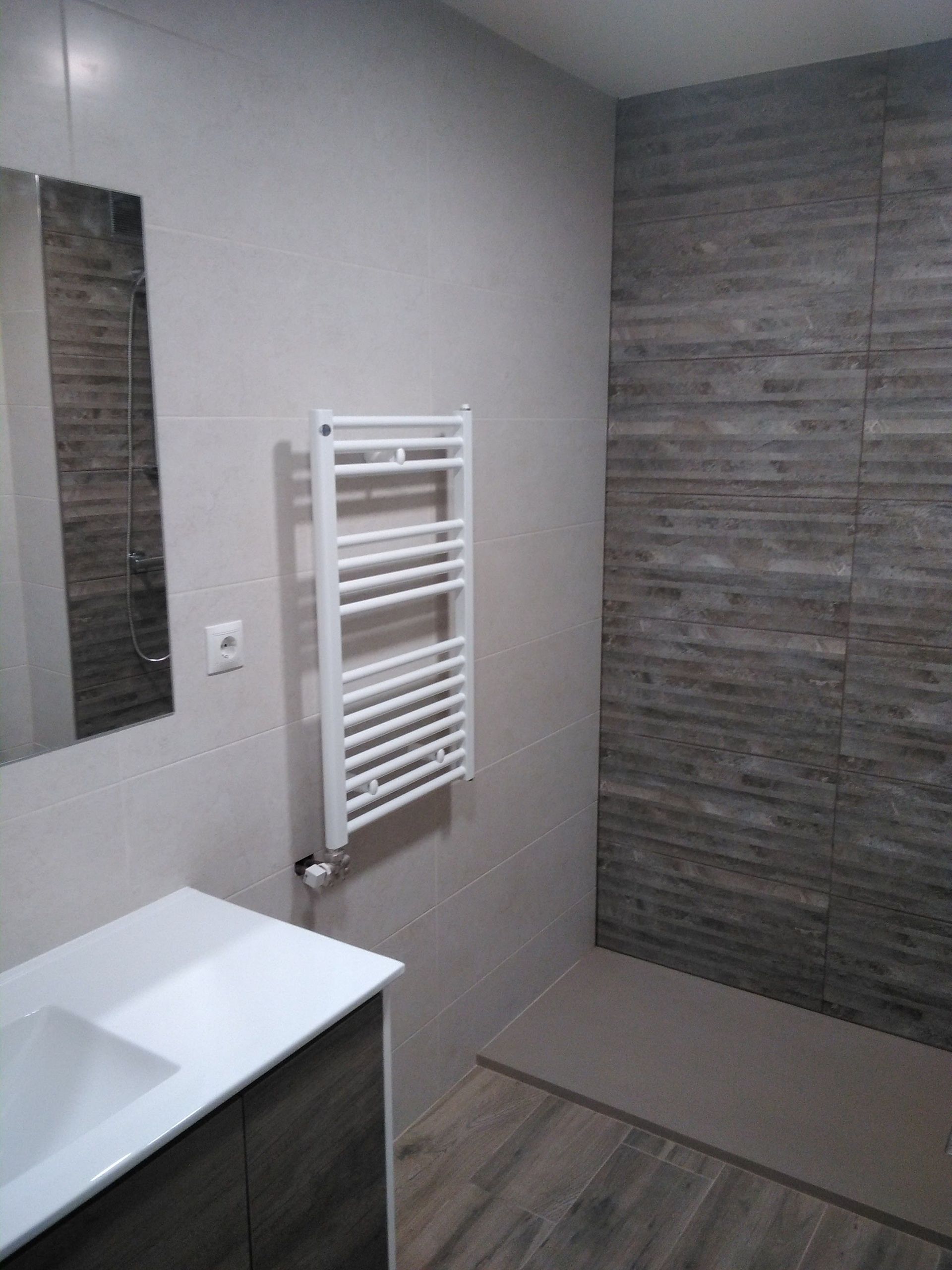 Baño moderno y pequeño con mueble de lavabo blanco, espejo de pared, toallero radiador blanco y pared de acento revestida