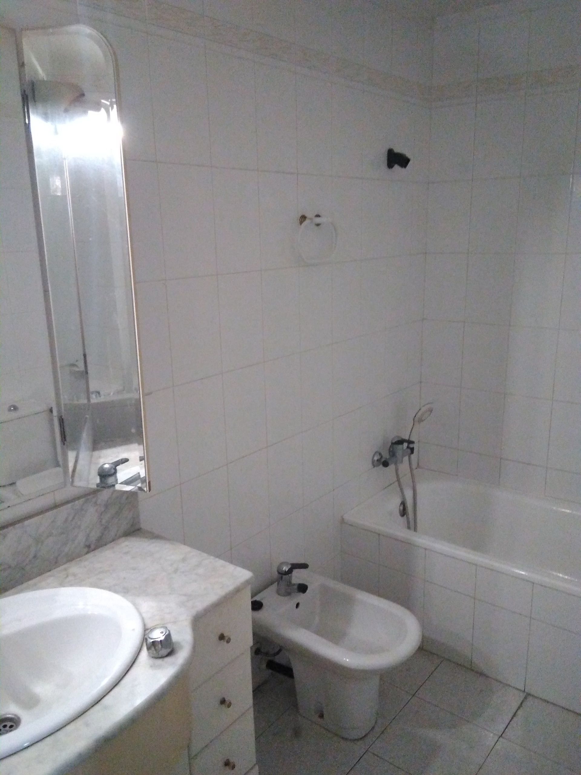 Baño pequeño con azulejos blancos, lavabo, bidé, bañera y espejo de pared.
