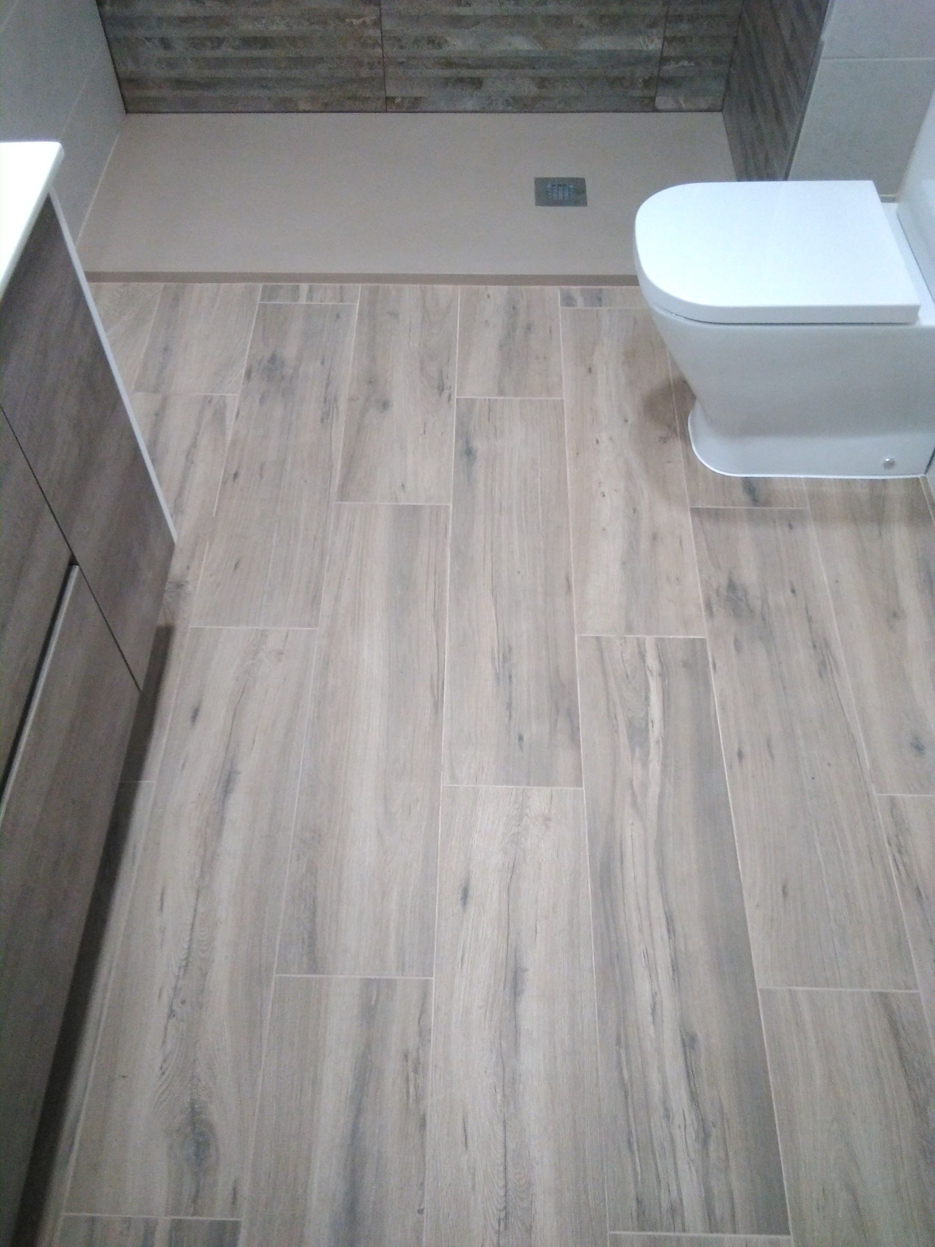 Baño pequeño con suelo de baldosas efecto madera, inodoro blanco y pared de ducha alicatada