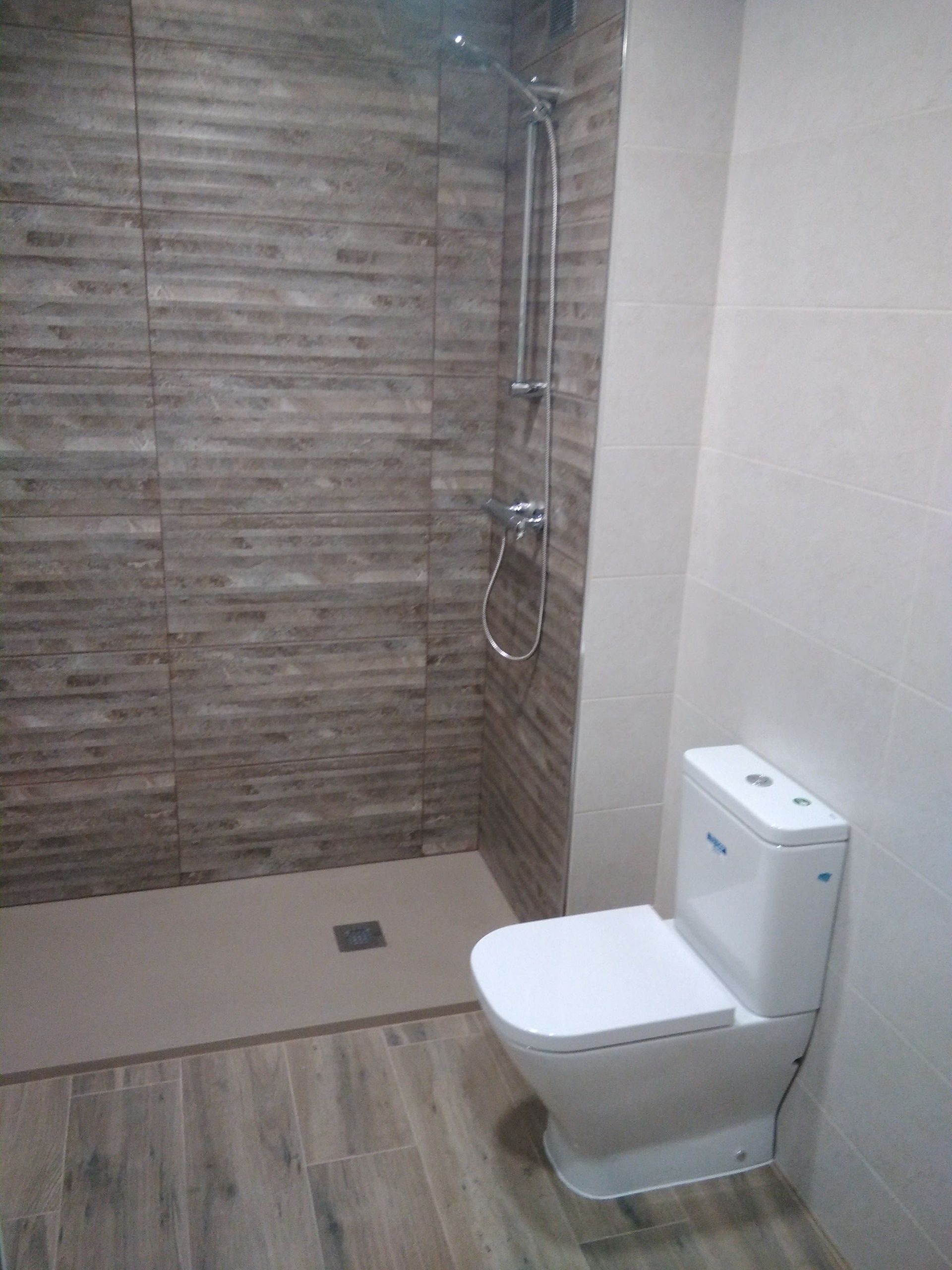 Baño moderno con un inodoro blanco y una ducha a ras de suelo alicatada.