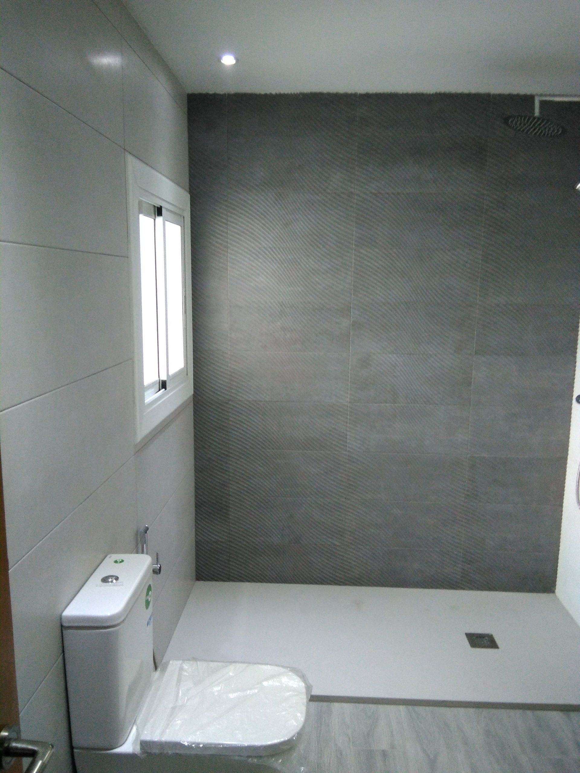 Baño moderno vacío con inodoro, ventana y ducha a ras de suelo con una pared de azulejos grises.