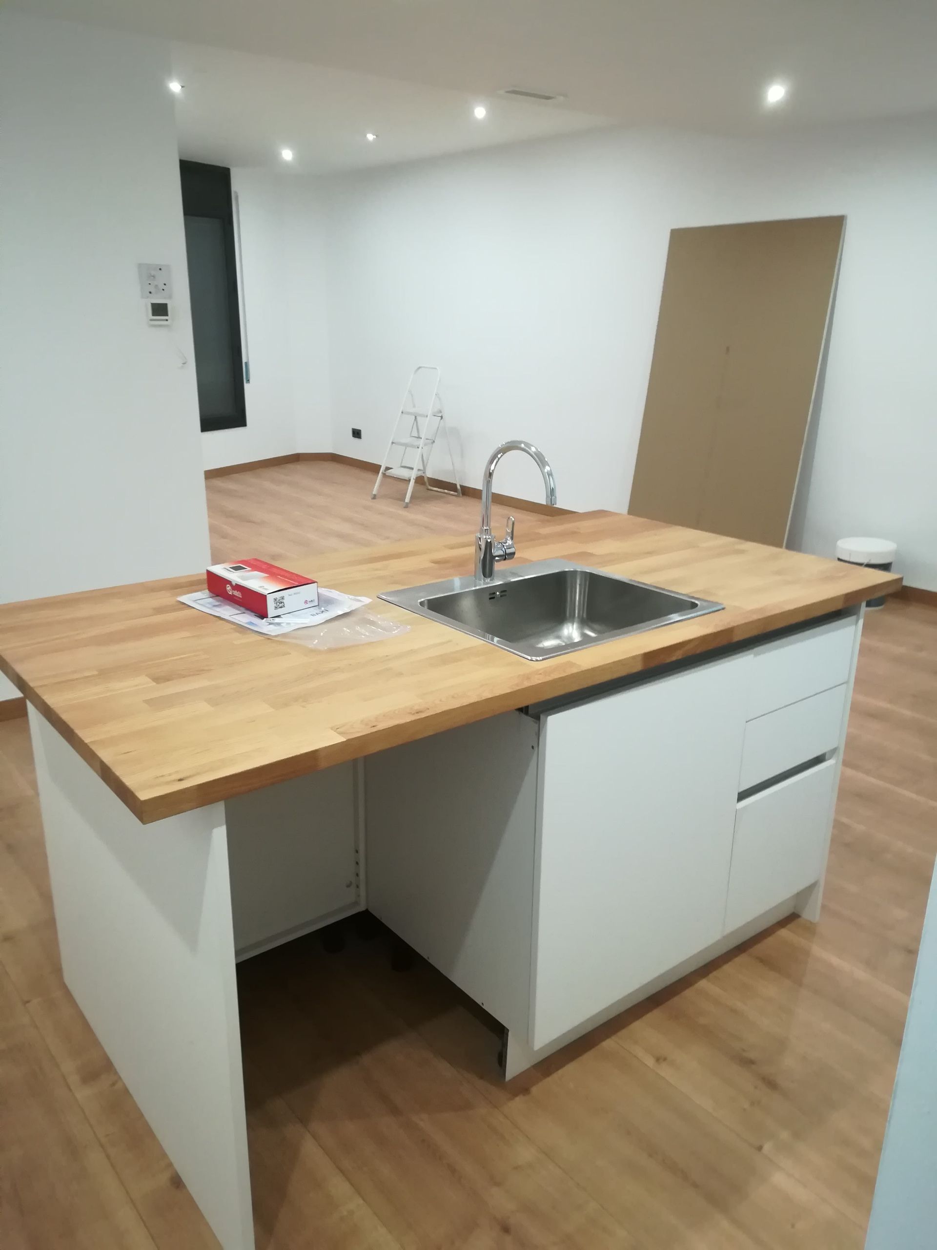 Cocina moderna vacía con armarios blancos, isla con encimera de madera y fregadero de acero inoxidable