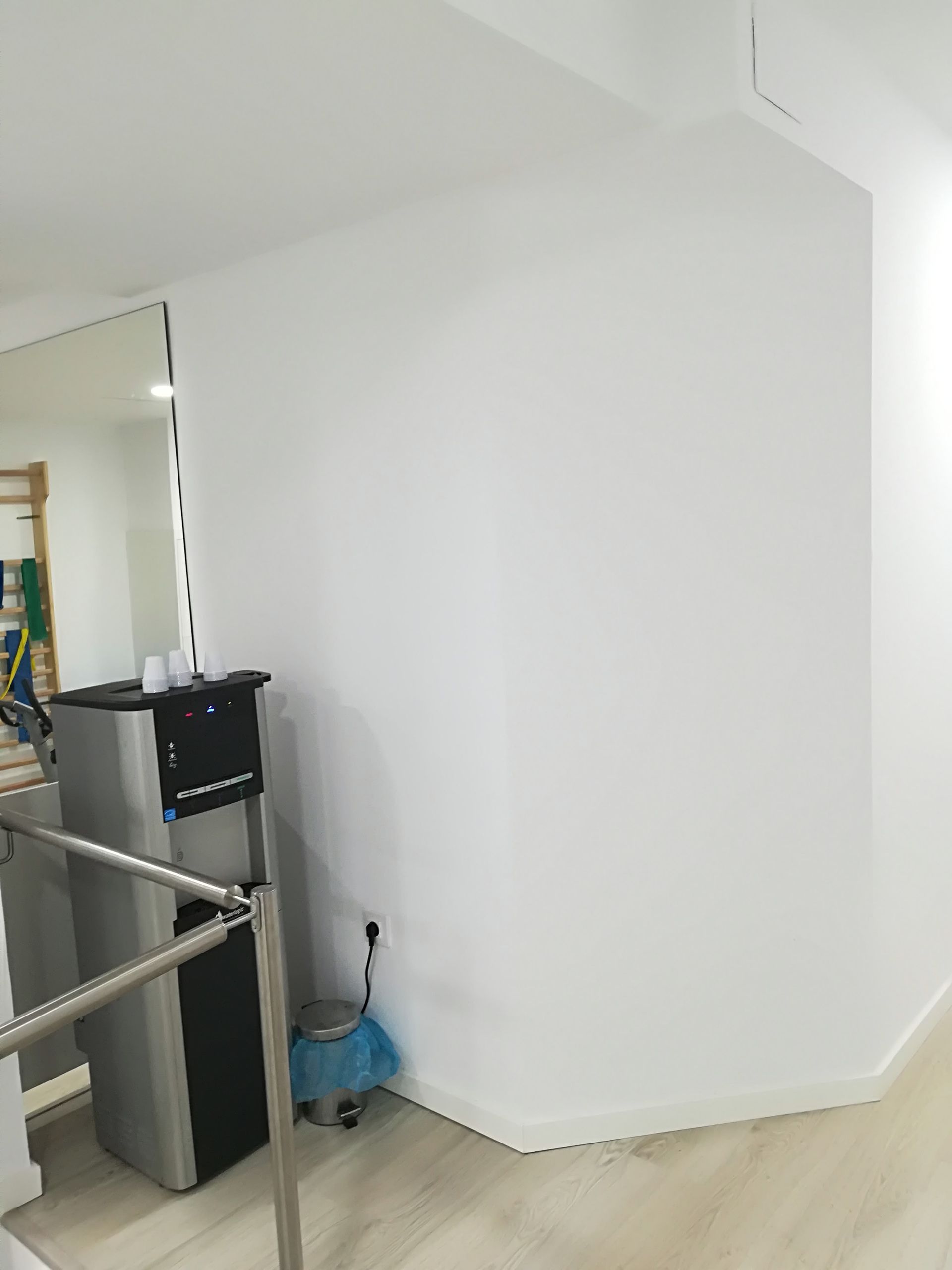 Rincón de una habitación blanca vacía, con un espejo, una escalera de mano y productos de limpieza en el suelo