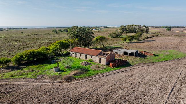 Casa de fazenda abandonada com telhado de telhas vermelhas em um campo rural seco e aberto sob um céu claro.