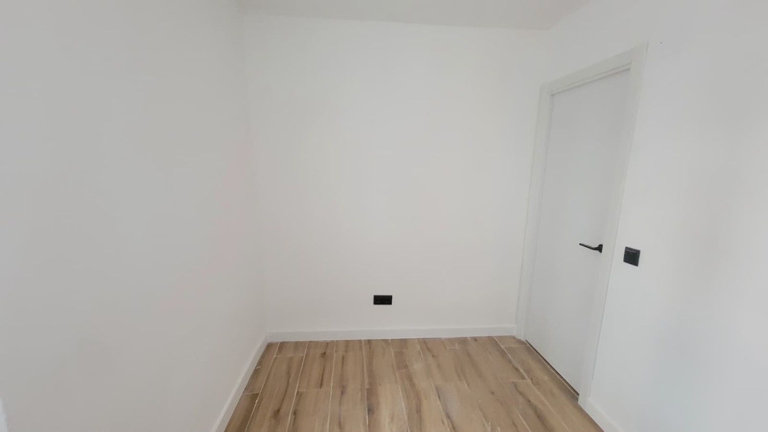 Una habitación pequeña con paredes blancas, suelo que imita la madera