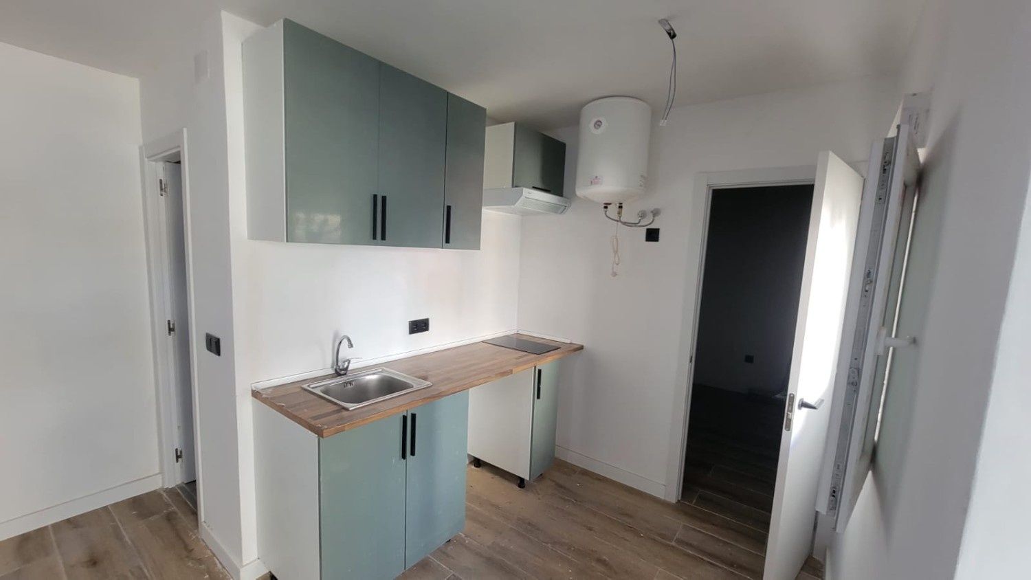 Una cocina compacta con armarios azul claro, encimera de madera, fregadero de acero inoxidable y calentador de agua mural.