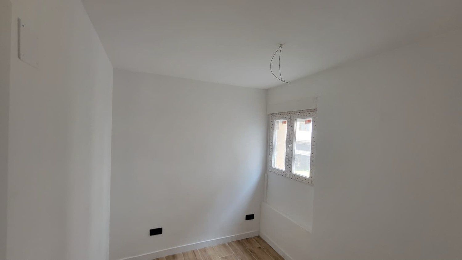 Una habitación vacía, recién pintada de blanco, con una pequeña ventana