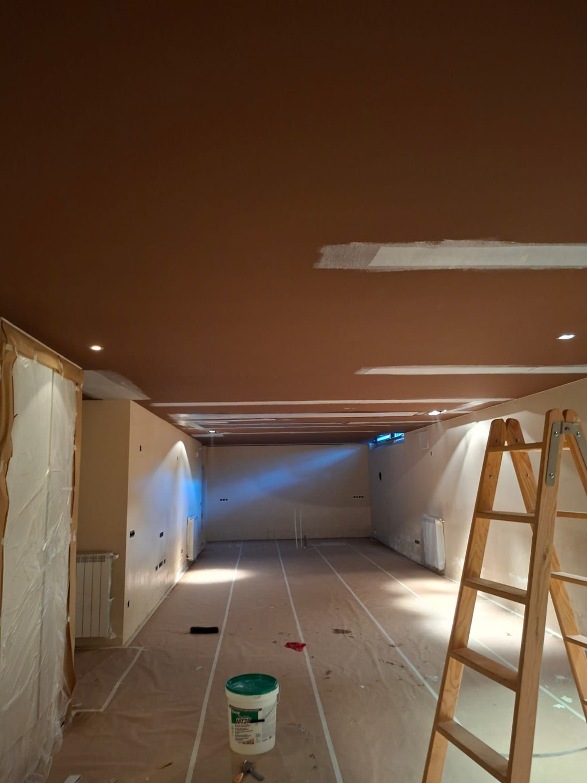 Hombre con ropa de trabajo blanca, respirador y casco en una habitación en construcción.