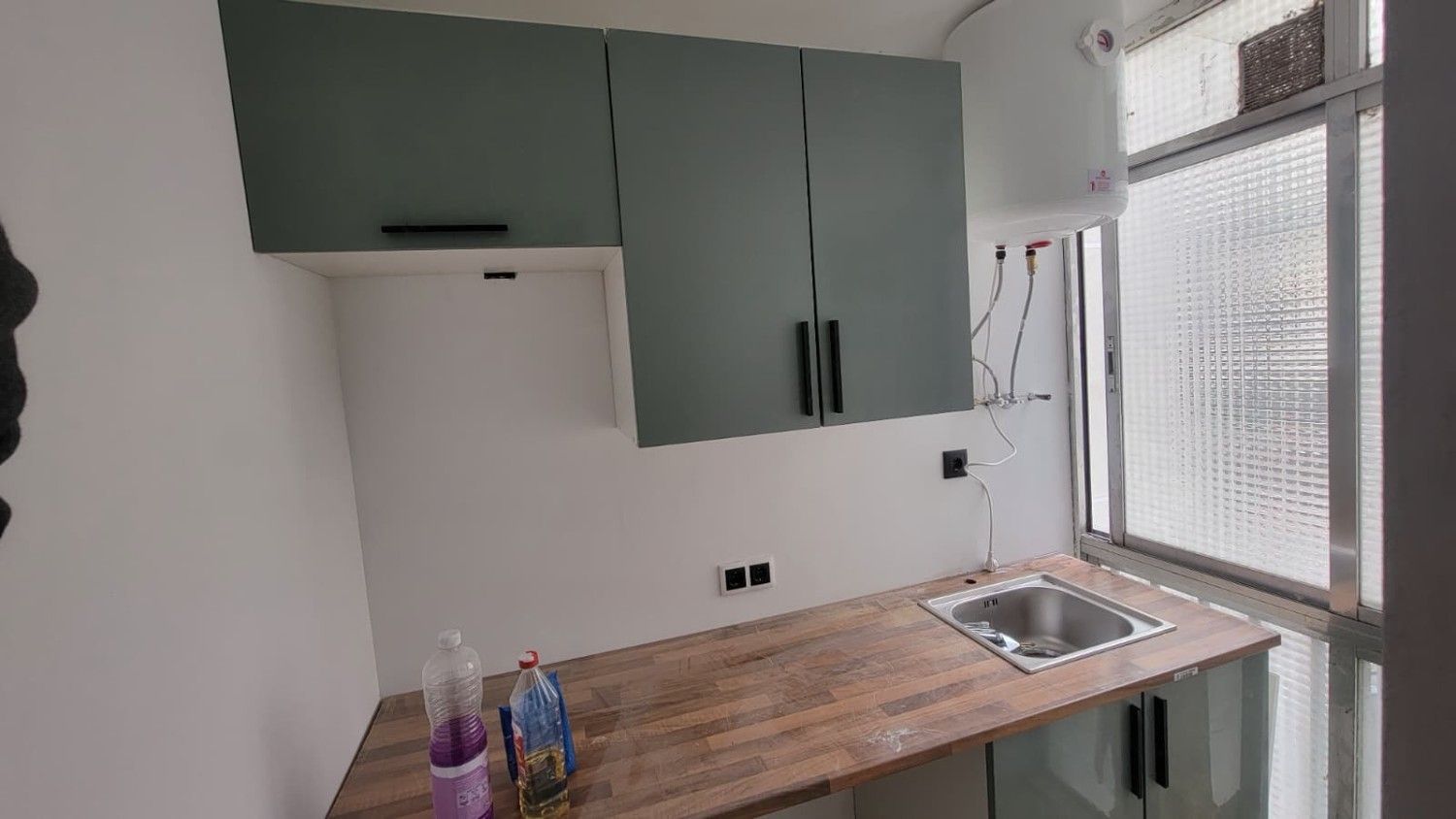 Una pequeña cocina con armarios superiores verdes