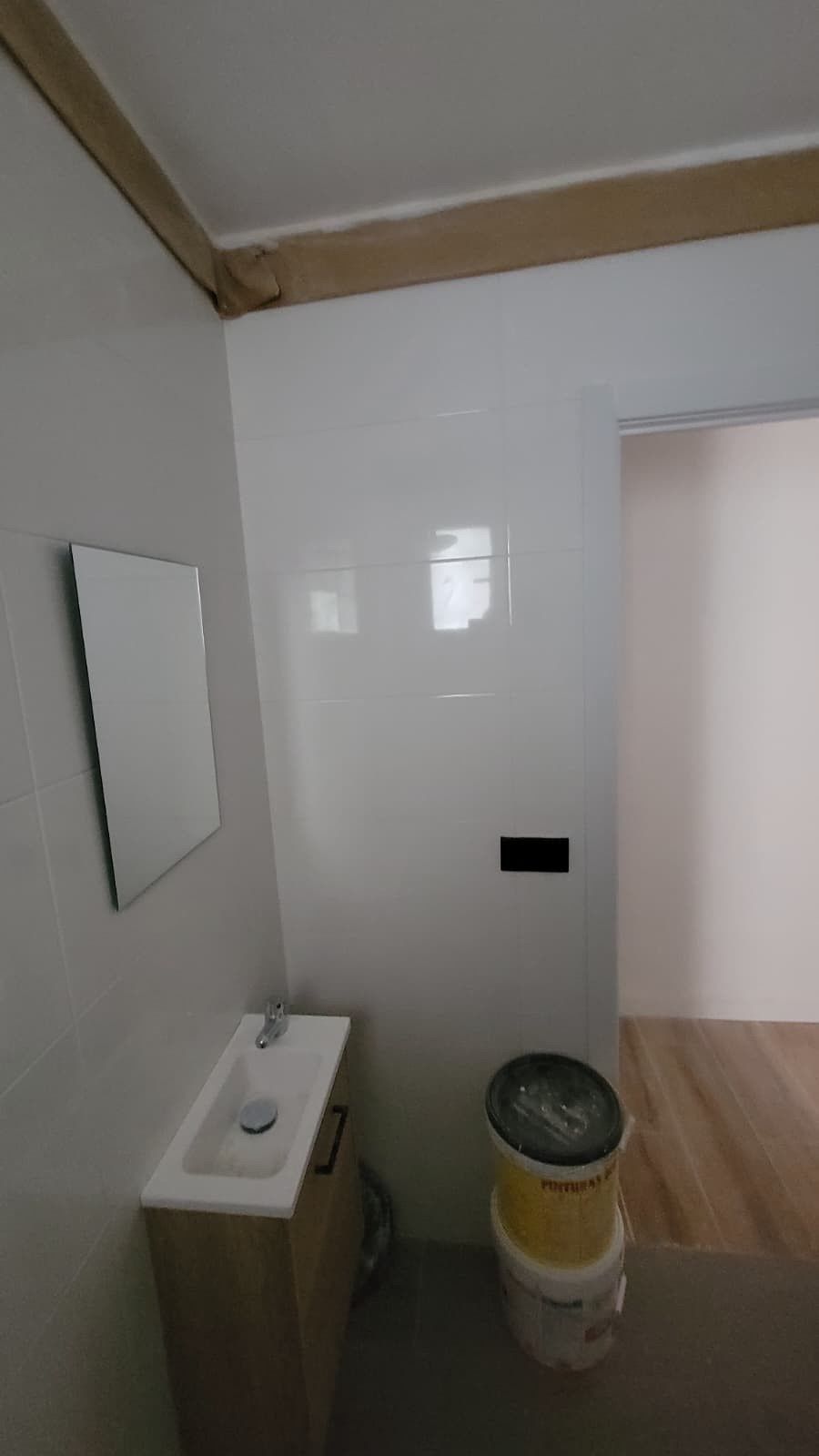 Un pequeño baño con tocador, lavabo blanco y espejo, junto a un inodoro portátil sobre un suelo gris.