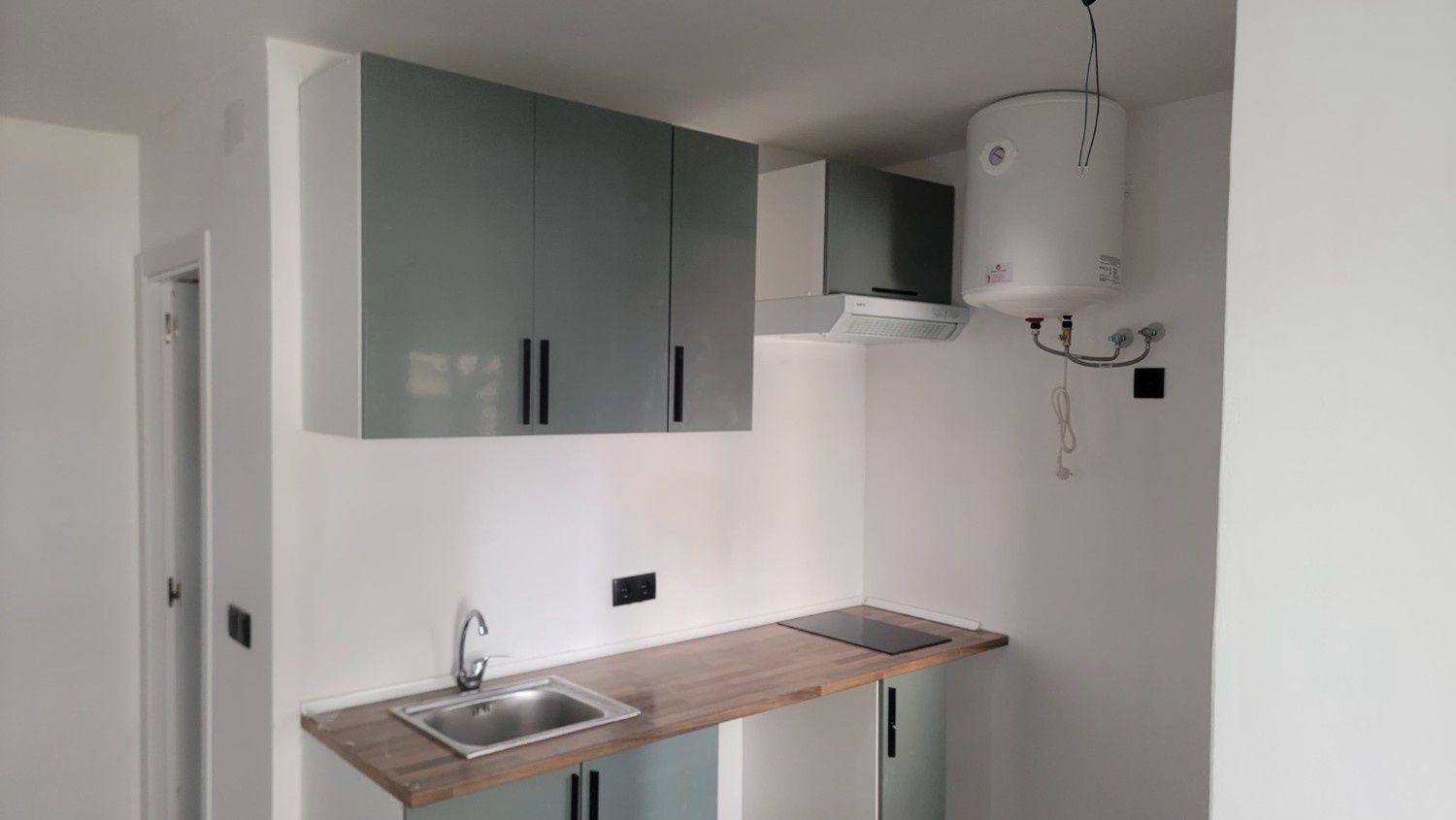 Una cocina moderna con armarios grises, encimera de madera, fregadero de acero inoxidable, placa de inducción y caldera.