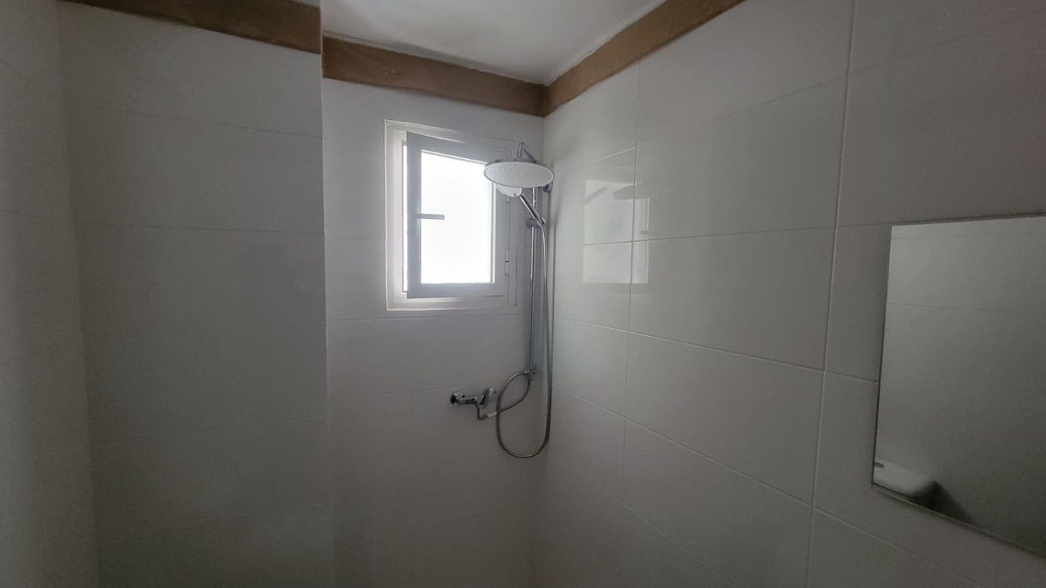 Una cabina de ducha con paredes alicatadas en blanco