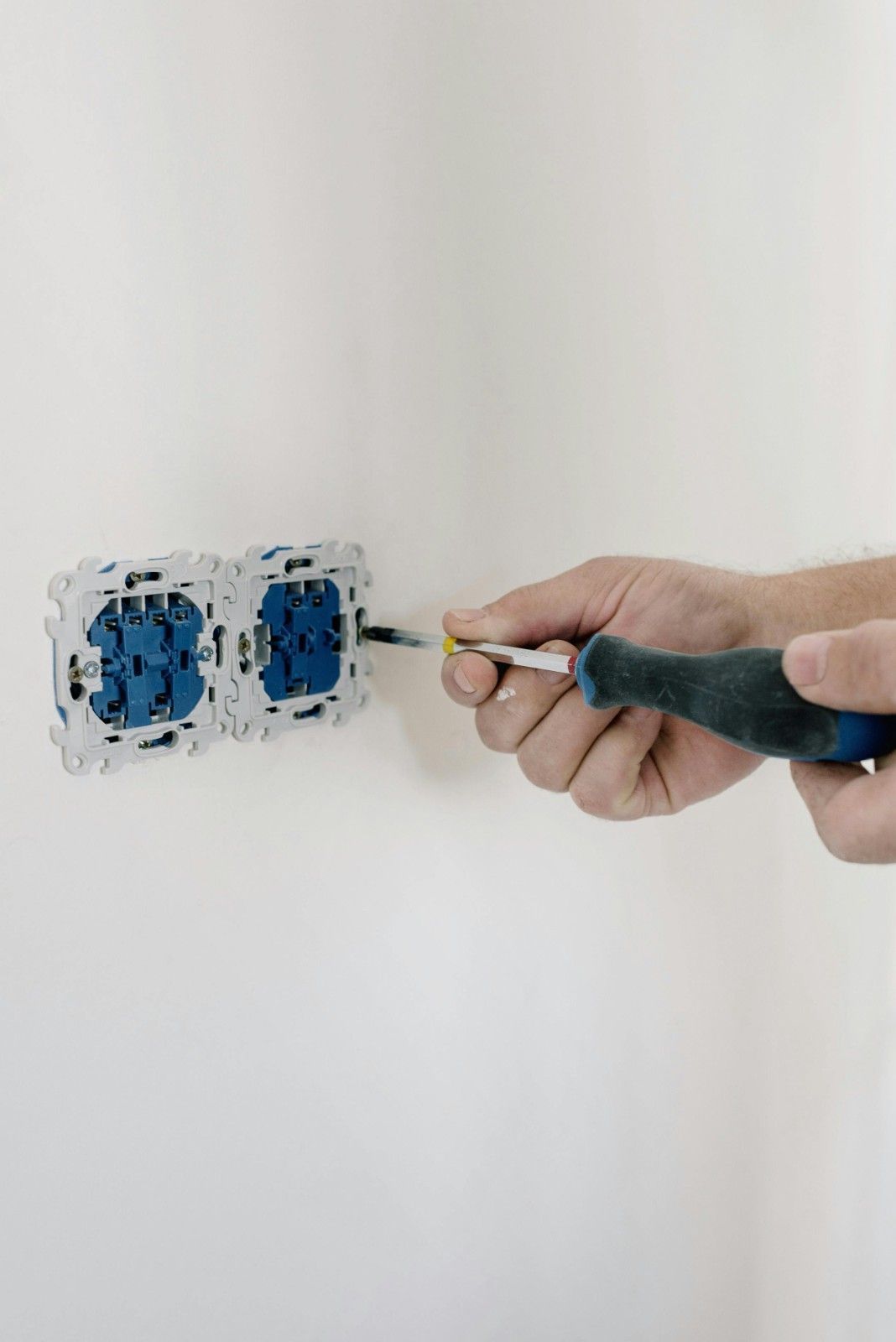 Persona que utiliza un destornillador para instalar un tomacorriente azul en una pared blanca.