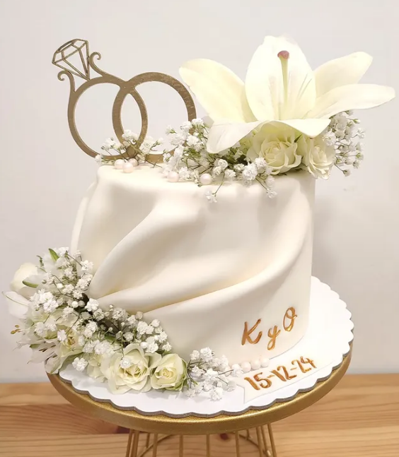 Un pastel de bodas blanco con flores y un anillo en la parte superior.